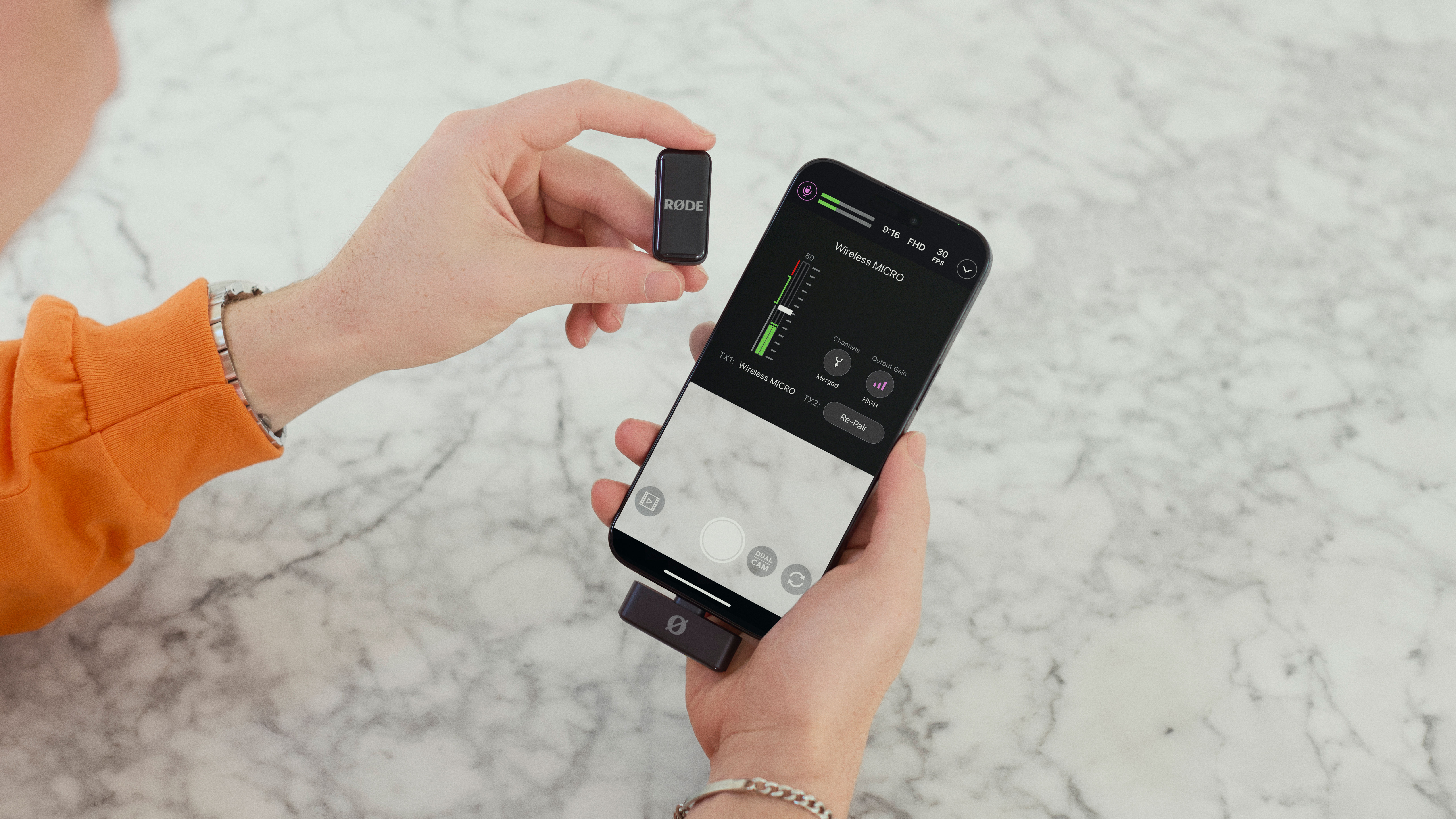 Rode Wireless Micro receiver connected to an iPhone held in a hand with a microphone held in the other hand over a marble surface