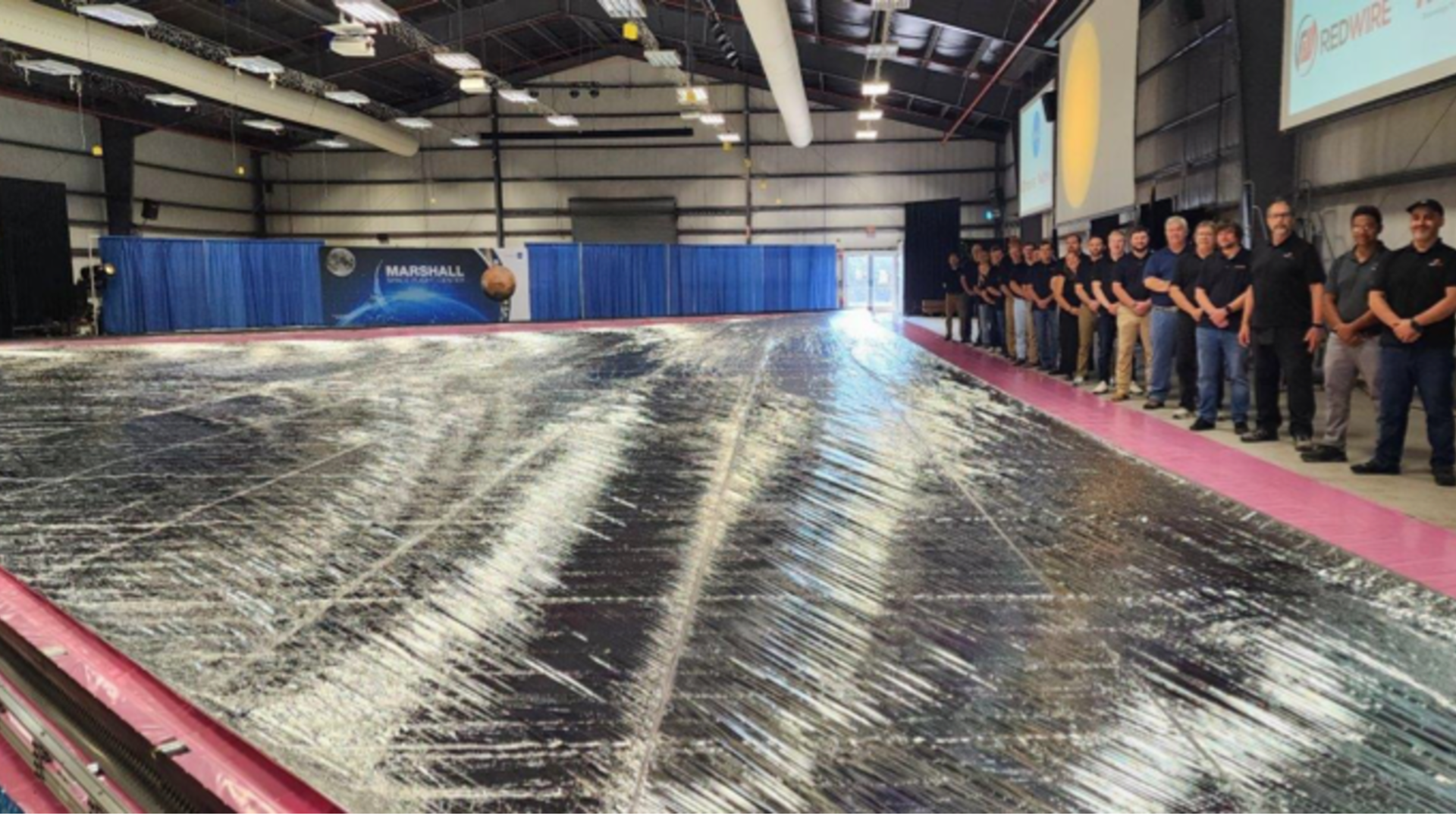 A line of NASA engineers posing with a silver solar sail.