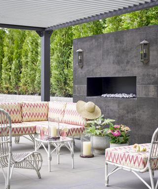 patio lighting ideas, purpose built outdoor fireplace with lantern style sconces, white rattan couch and chairs, planters, coffee table, candlelight