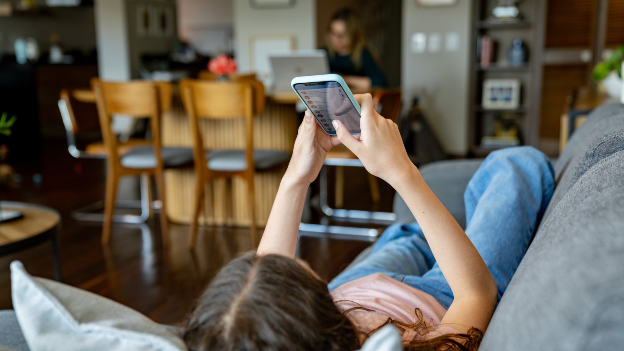 A stock photo of a girl sitting on the couch using her cell phone. 