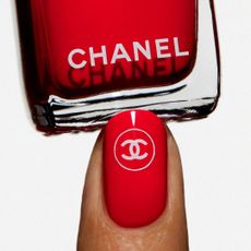 red Chanel le vernis polish with one finger coated in red polish with a white Chanel nail sticker