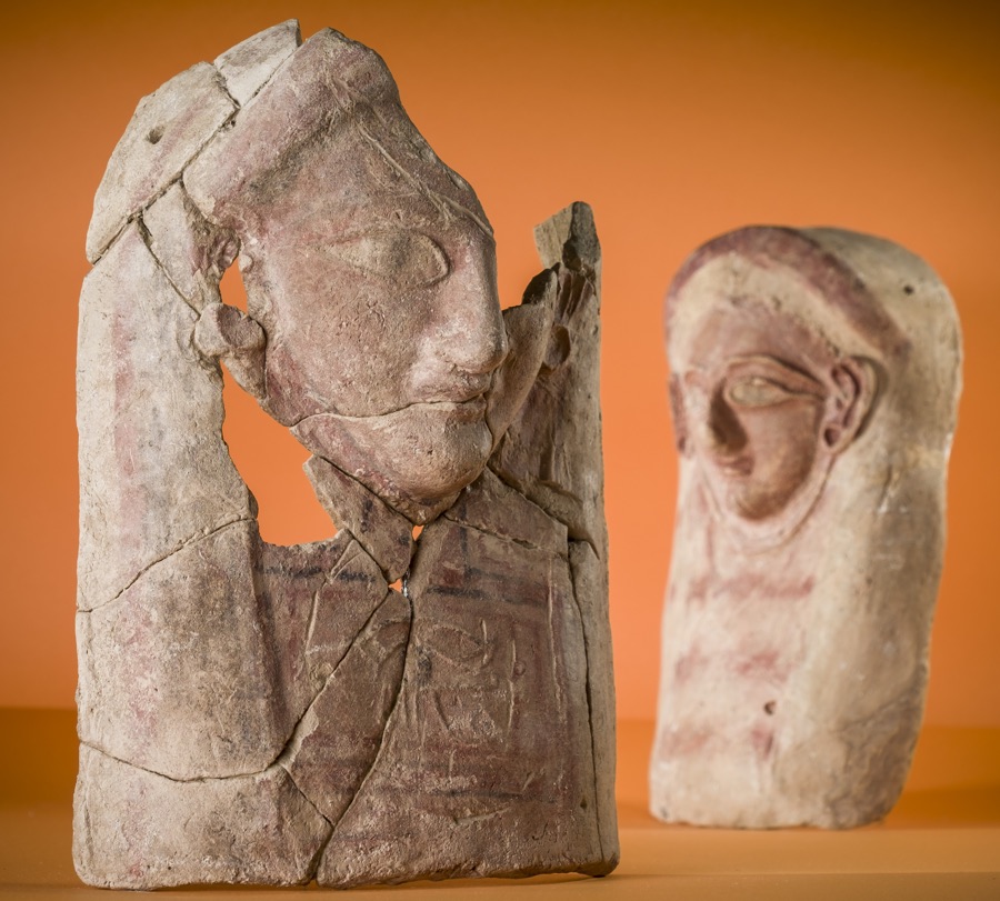 The head at left has an image of a wadjet amulet on its breast. Wadjet amulets show an eye and are of Egyptian origin.