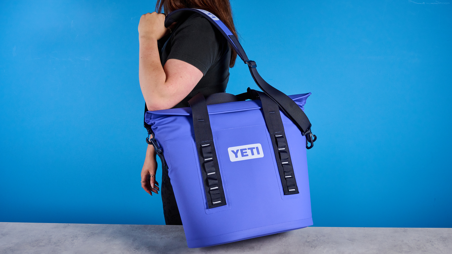 the yeti hopper m15 cool bag with a padded carry strap, handles, and a 15 quart capacity photographed with coke zero cans against a blue background