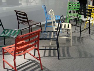 Multiple straw chairs in red, green, white, black and blue photographed on a grey surface next to a glass wall