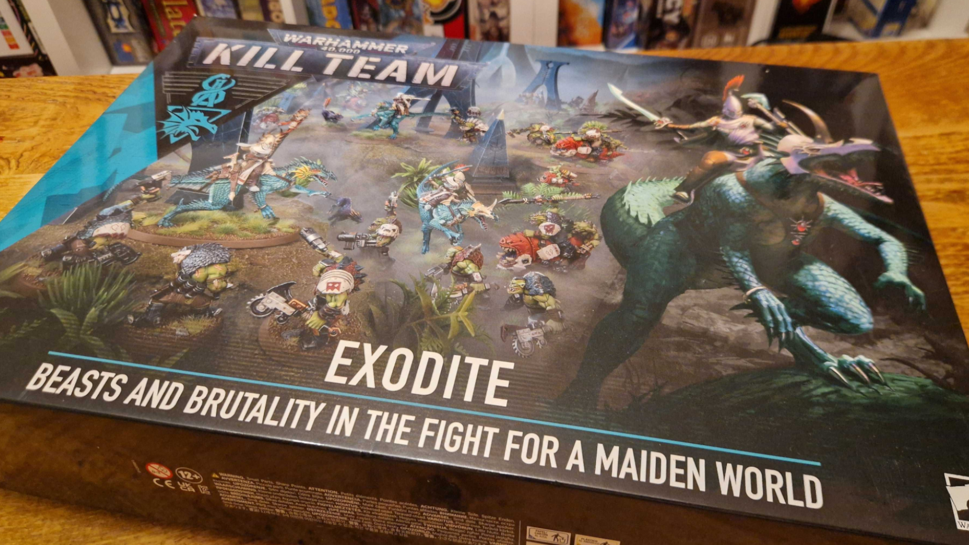 A Kill Team: Exodite box laid out on a wooden table in front of board games