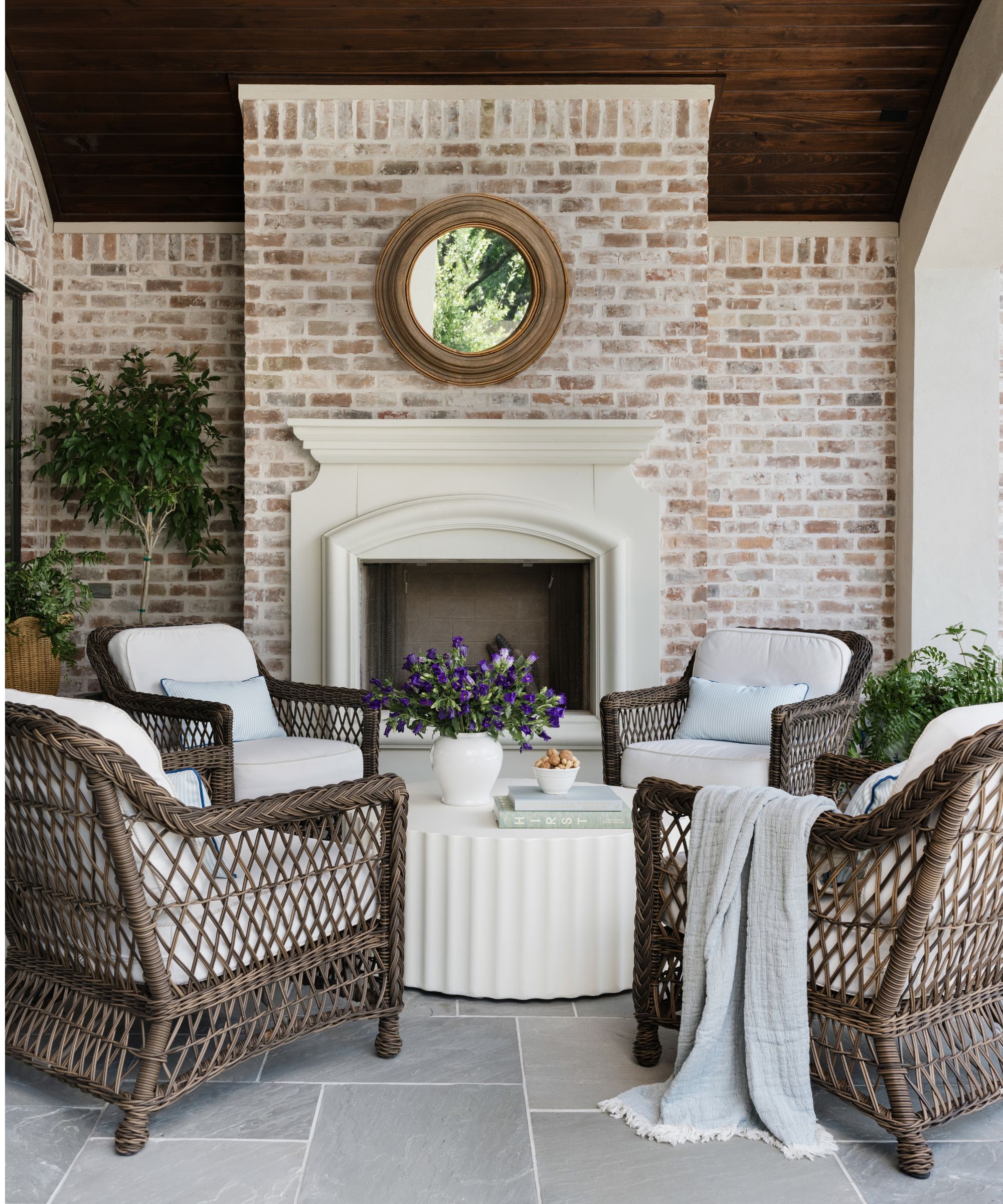 a covered patio area with wooden ceiling, brick walls and fireplace with a circle coffee table and wicker chairs