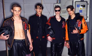 4 male models in black & orange clothing posing for the camera