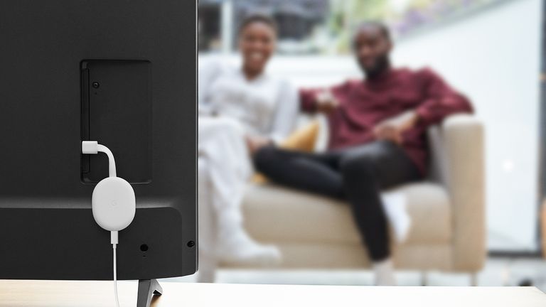 Close up of one of the best Chromecast device plugged into TV with blurred couple on sofa in the background