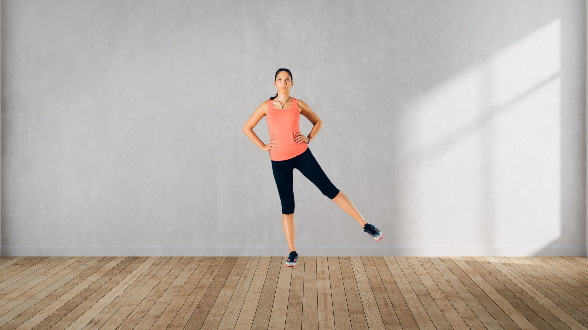 Woman stands with her back to a wall, hands on her hips and a leg raised to one side