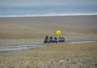 Five members of the Haughton-Mars Project traverse an Arctic landscape on ATVs.