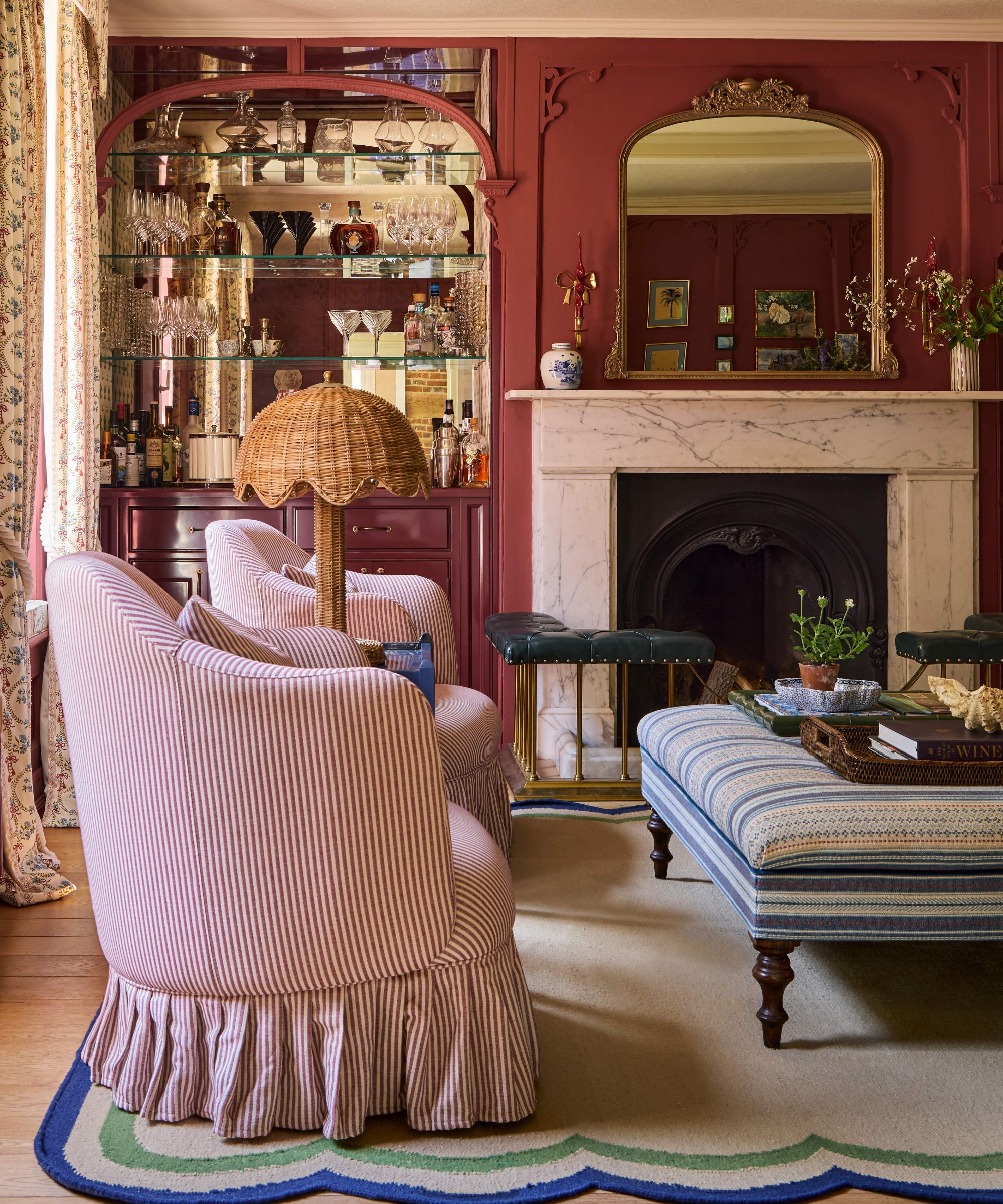 a reddy pink painted drawing room with ornate moldings, a custom mirror arched home bar and a marble fireplace