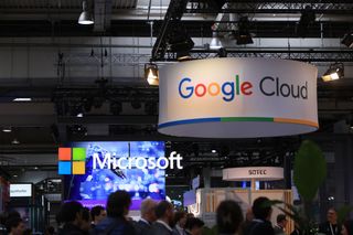 A photo of a conference show floor with a Microsoft and Google Cloud sign hanging above attendees