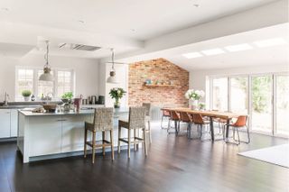 a modern bright kitchen extension, with a dark wood floor, a white kitchen island and white cabinets, a large dining table and bi-fold doors
