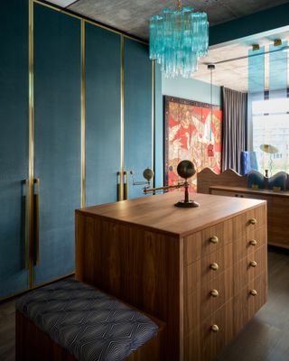 Dresser area of bedroom with teal velvet wardrobe doors, wooden chest of drawers and aqua Murano glass chandelier