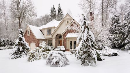 Suburban house with snow on the ground and more falling