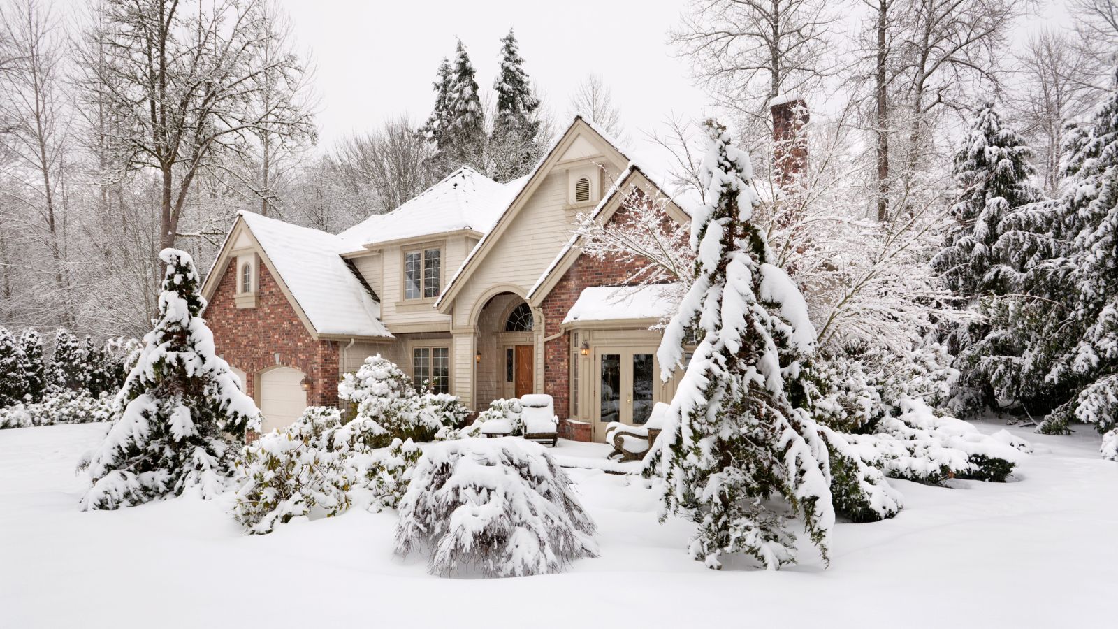 Suburban house with snow on the ground and more falling