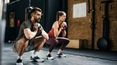 A man and woman doing a weighted cardio workout, performing a goblet squat with a kettlebell