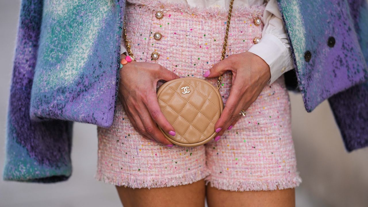 Maria Rosaria Rizzo wears a white with lace pattern oversized blouse / shirt from La petite Étoile, a beige shiny leather circle crossbody bag from Chanel, white and pale pink tweed high waist shorts from Édouard Achour, a blue and purple gradient print pattern fluffy / wool jacket from Tesei, during a street style fashion photo session, on April 20, 2022 in Paris, France.