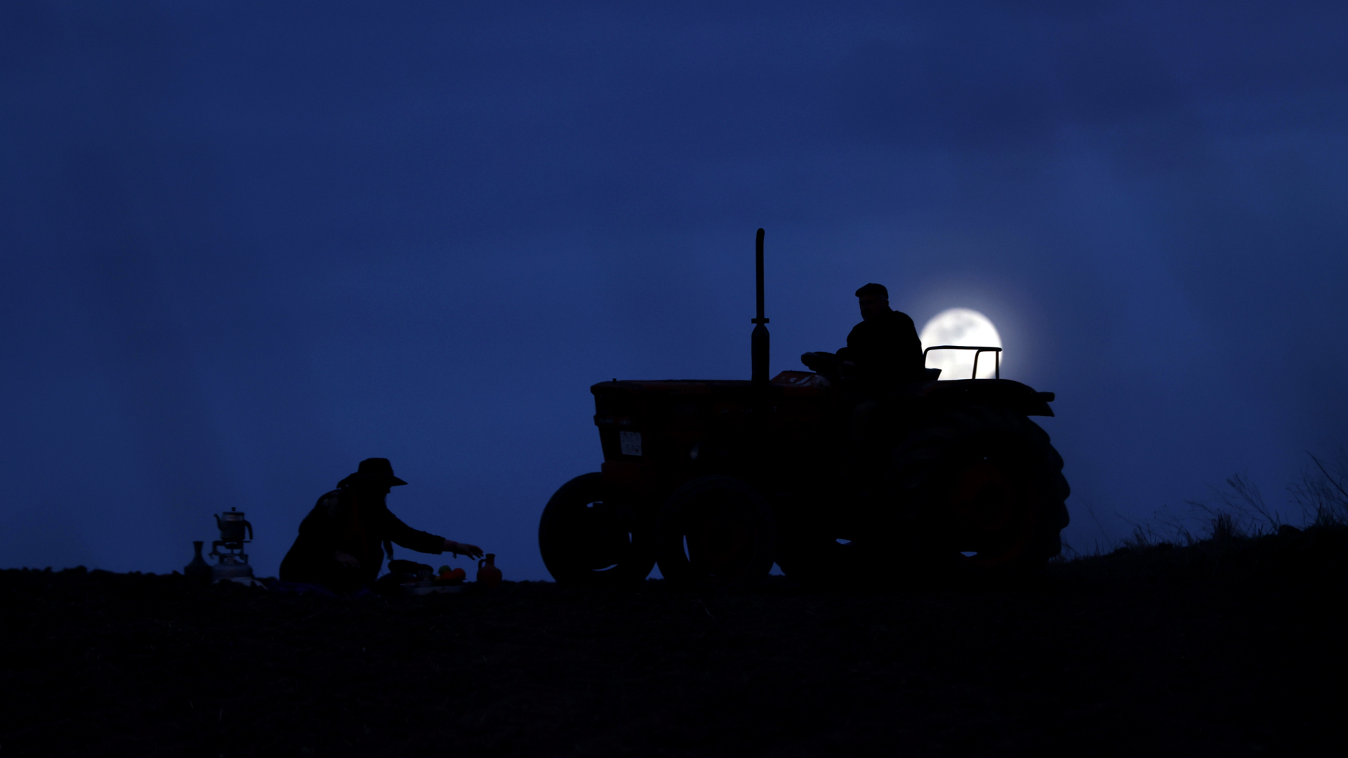 Silhouette of farmers with a full moon shining bright in the background.
