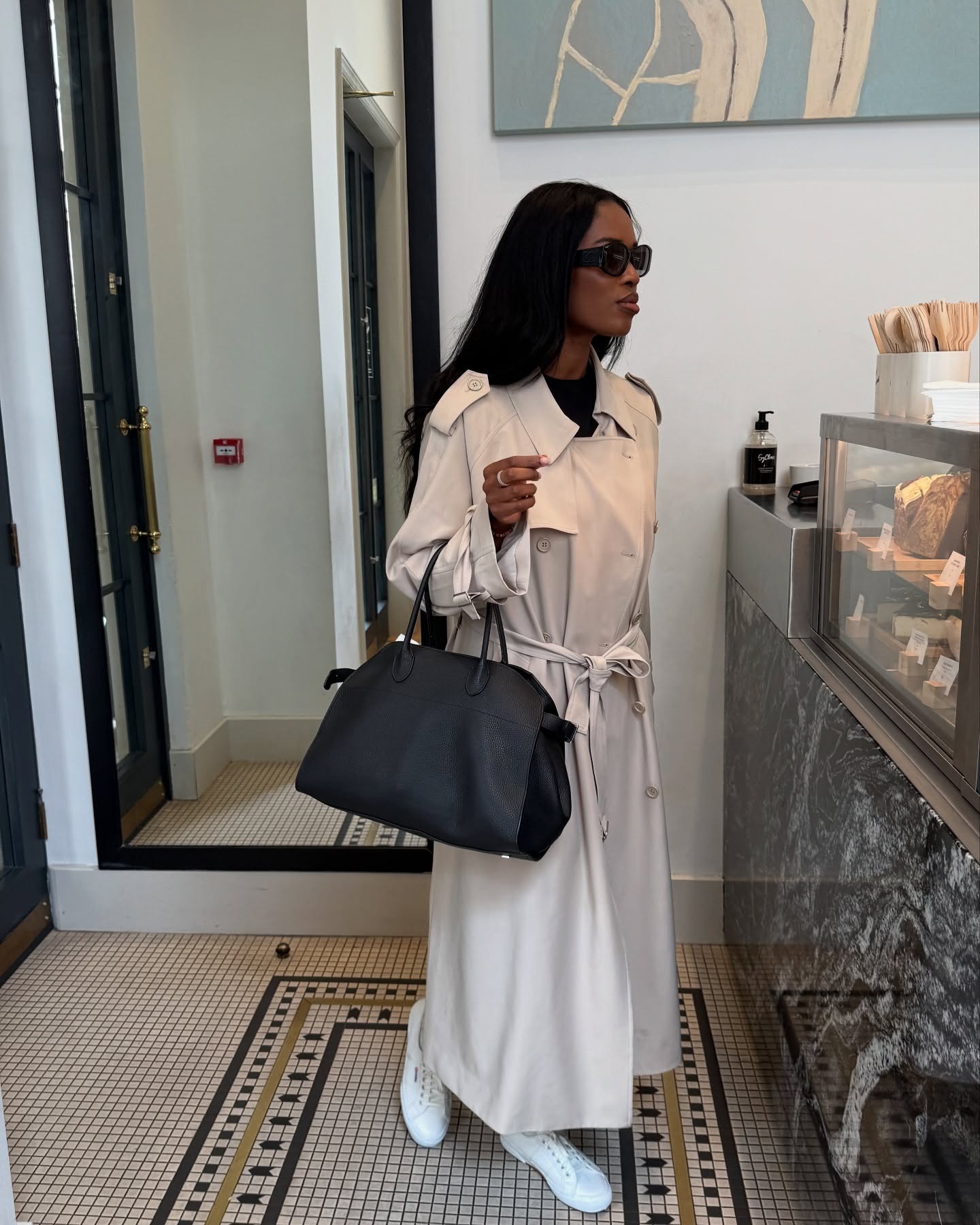 @nlmarilyn wearing a long trench coat, The Row Margaux bag, and white sneakers.