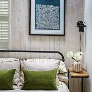 A bedroom with natural-style vertical wall panelling and striped bed linen on the bed