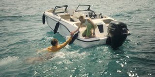 Miranda (Elen Rhys) is kneeling at the back of a powerboat, reaching out a hand to Max (Julian Looman) who is swimming in the sea fully-clothed