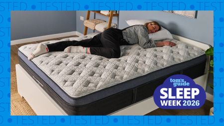 Tom's Guide Sleep Editor Nicola Appleton sleeps on the Helix Midnight Luxe, a mattress she still rates as the best mattress for side sleepers after sleeping on it for two years and re-testing it three times. Here Nicola is dressed in bed socks, a gingham shirt, black dungarees, and is lying with her head on a white pillow. Blue text containing the word 'Tested' wraps around all sides of the photo, with a Tom's Guide Sleep Week 2026 badge overlaid in the bottom left hand corner.
