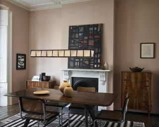 A dining room idea with earthy blush pink walls, abstract art on the walls and low tiled glass pendant bar light over dark brown table