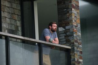 Miles (James McArdle) stands on the balcony of his impressive but austere-looking house, which is contructed of black metal and slate-coloured bricks. He is leaning on the barrier and resting a cup of tea on it as he looks out at the horizon.