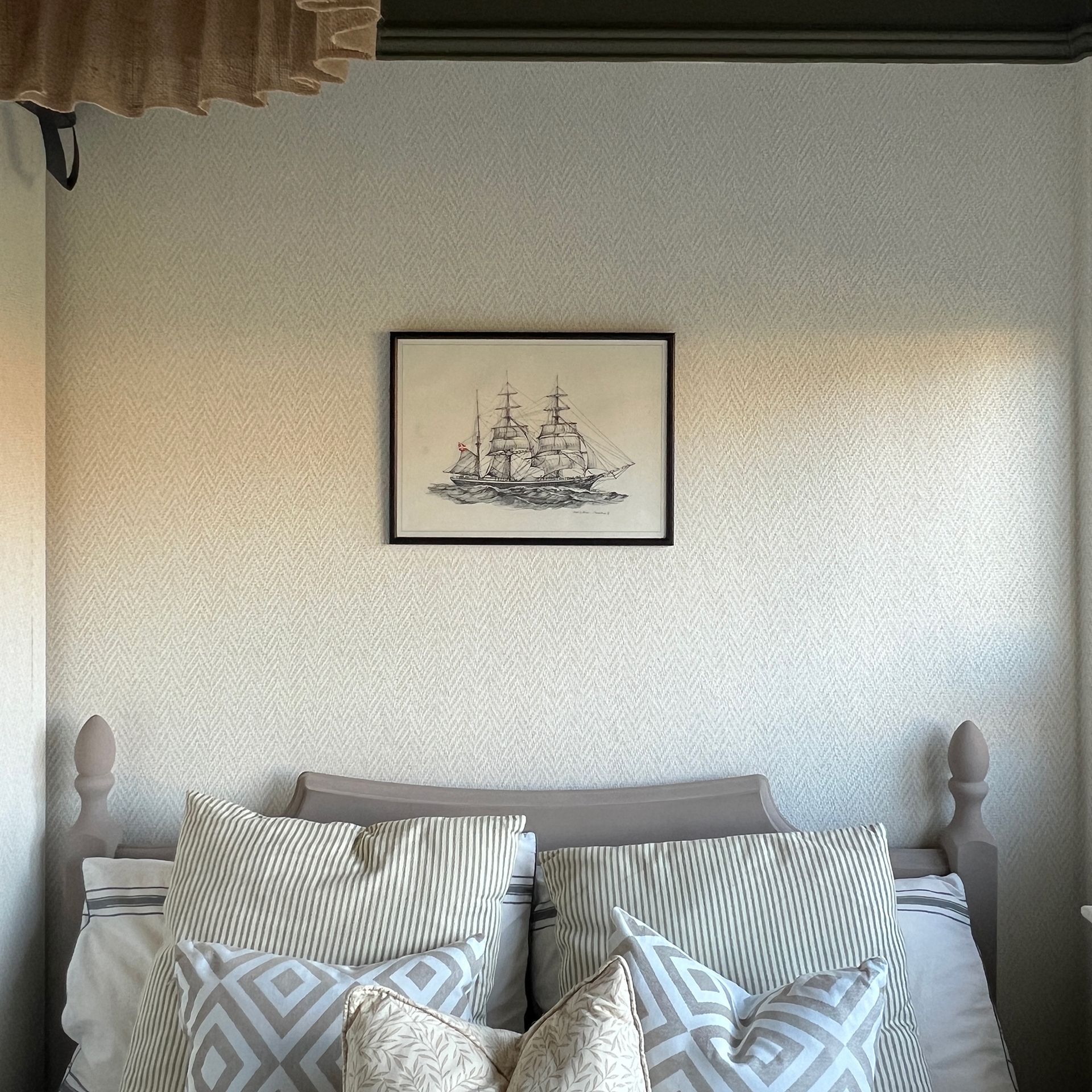 Neutral bedroom with framed drawing of shop above bed with patterned throw pillows