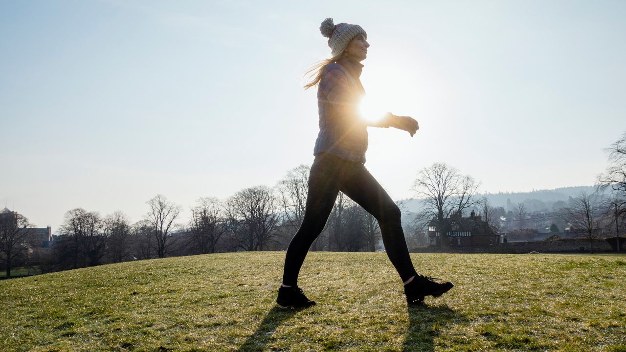 A woman walking in the sun, wearing a bobble hat