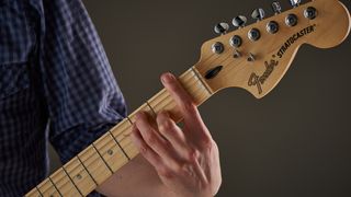 Close up of man's hand playing F chord shape on electric guitar