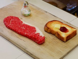 A slice of toast with a knob of butter and a scoop of jam, next to a salt shaker and a piece of raw meat