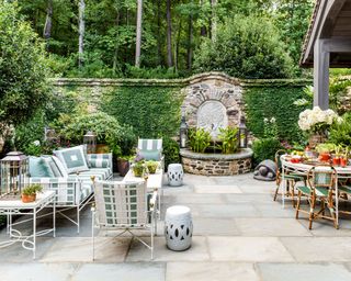 large flagstone patio with two seating areas and a water feature in the stone wall