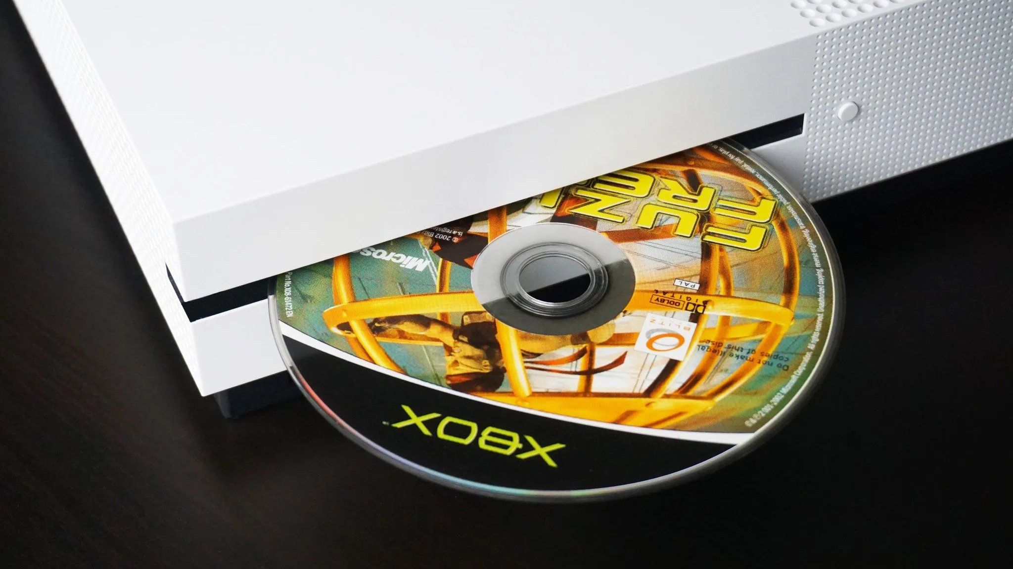 Original Xbox game disc being inserted into a white Xbox One S console, highlighting physical game media and disc-based gaming.