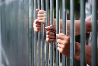 Women's hands hold the bars of a prison cell.