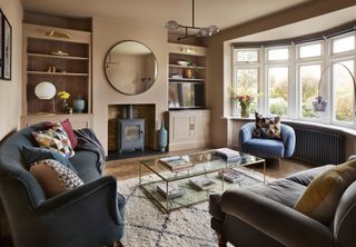Dani Ellis home: living room with subtle pink walls, shelving built into alcoves either side of fireplace, plush sofas and a glass and brass mid century style coffee table
