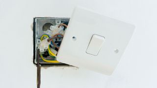 Standard white plastic light switch cover hanging off wall via wiring 