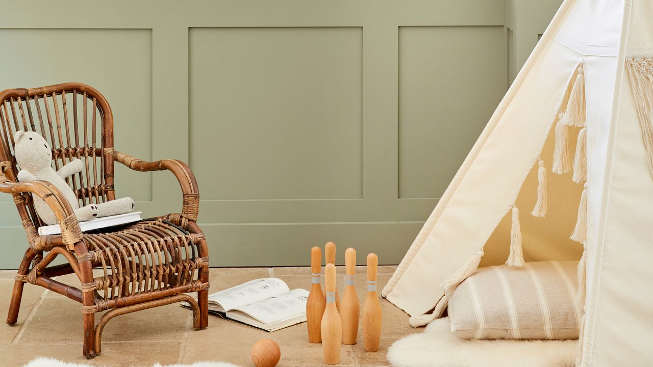 Sage green walls, wooden floor, wicker chair with teddy, wooden skittles and white tent