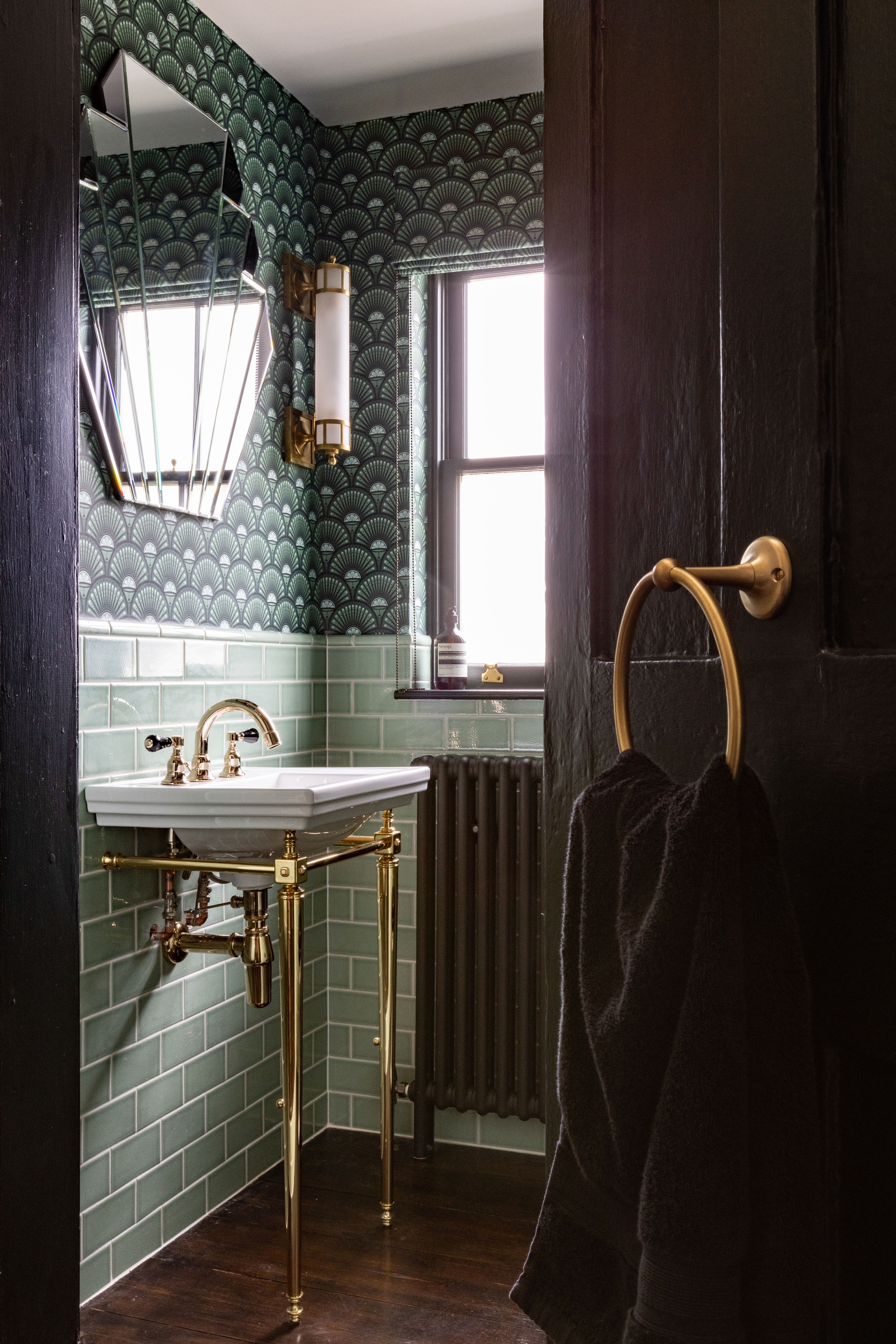 a dark green art deco bathroom with wallpaper, tiles and an fan shaped mirror