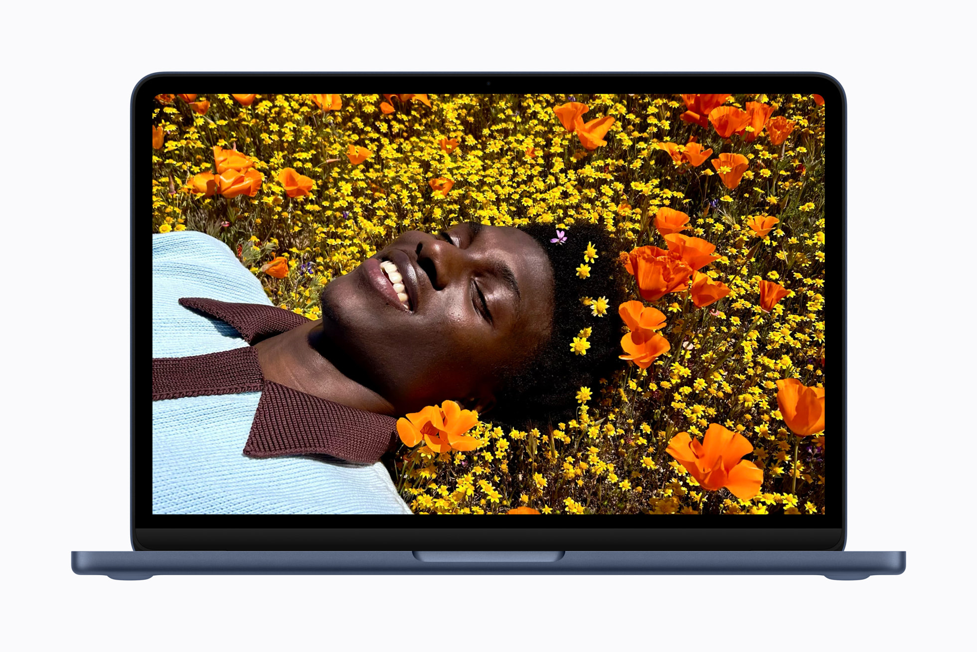 A dark blue laptop displays a full-screen photo of a person smiling while lying in a field of bright orange and yellow flowers.