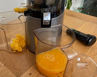 Mid-process of juicing oranges in Hurom H-AA slow juicer, pulp extraction shown with juice yield in jug