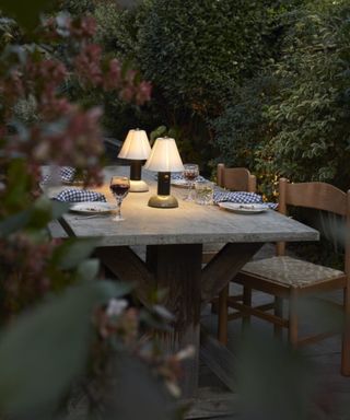 marble table surrounded by hedges with a tablescape with two portable lamps