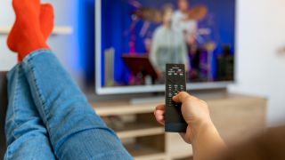 Person sitting with their feet up on the sofa with remote control in hand, watching musicians on TV