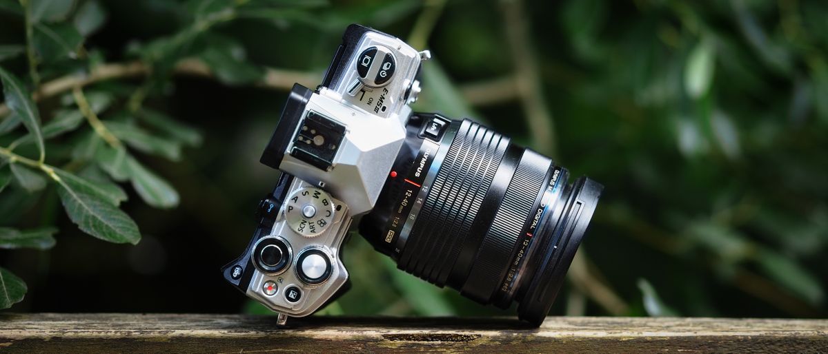 Olympus M.Zuiko 12‑40mm f/2.8 Pro lens on a wooden surface in front of green foliage