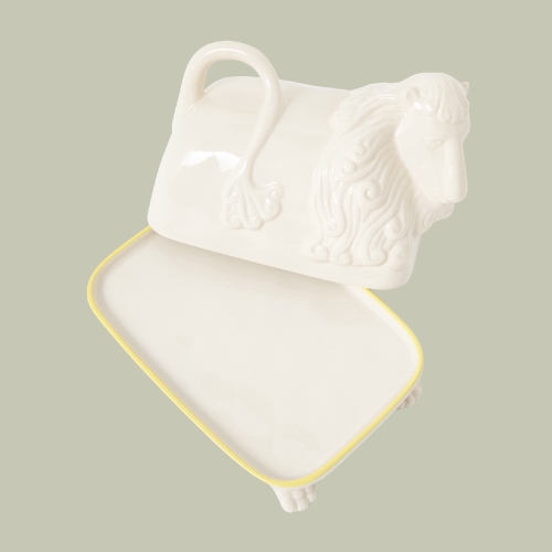 a white butter dish that is shaped like a lion on a sage green background