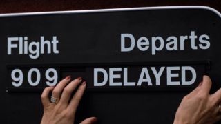 A hand placing a "delayed" sign next to flight 909 in Planes, Trains and Automobiles