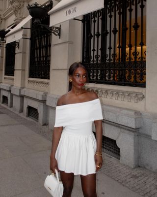 The influencer wears a white handbag with a white off-the-shoulder mini dress.