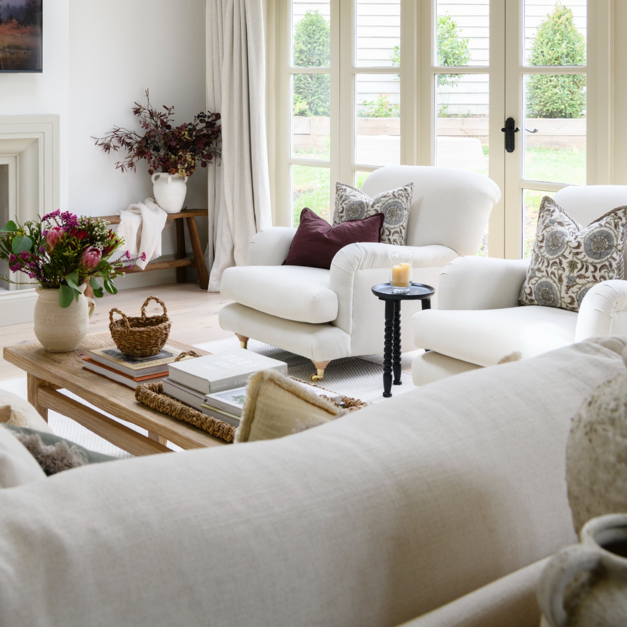 A white living room with two white armchairs with contrasting scatter cushions