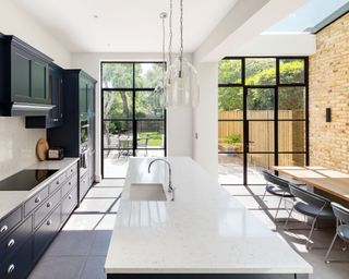 A large kitchen with black cabinets and a white island in front of glass doors with black frames